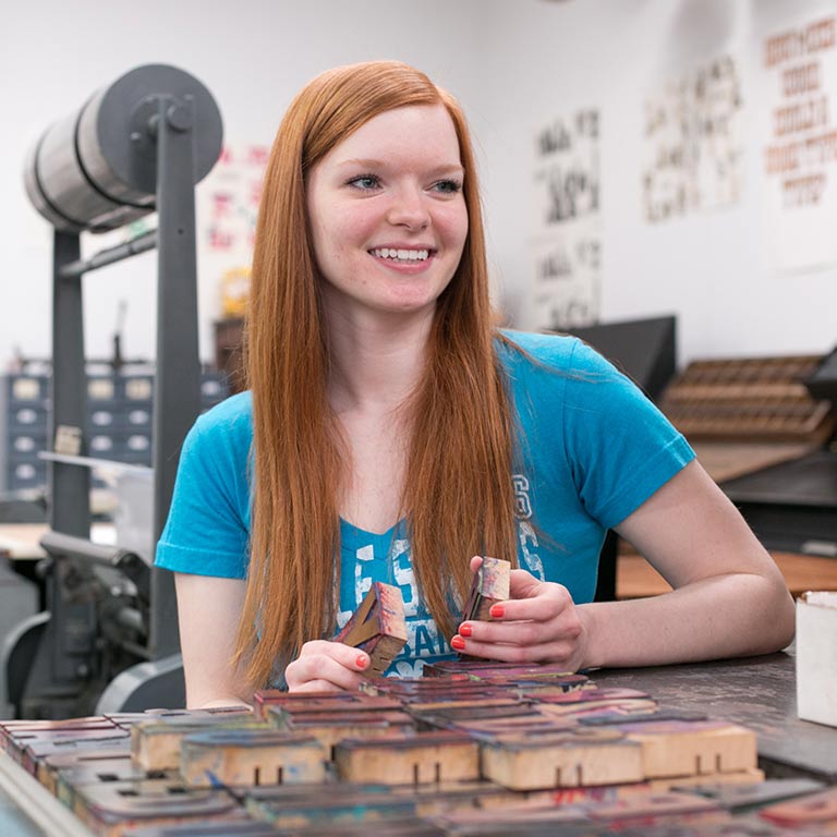 A student smiles as she works with letterpress.