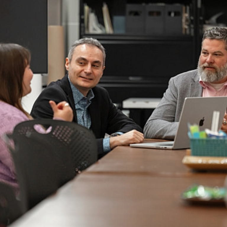 Three IU Indianapolis faculty members sit at a table and smile while dicussing a collaborative project