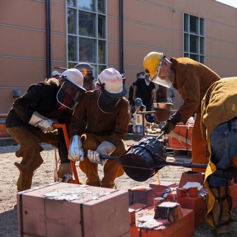 Group of Herron School of Art and Design students working together in protective clothing to pour molten iron into a mold