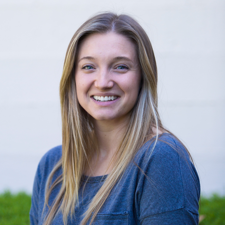 A headshot of Ashleigh Mower smiling and wearing a blue shirt while standing outdoors.