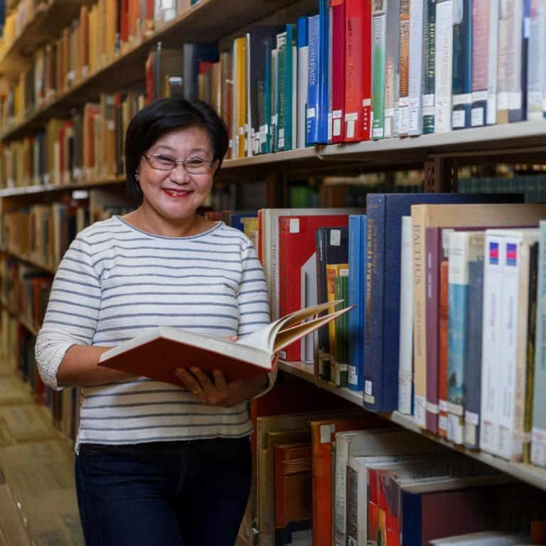 Art history professor Uranchimeg Tsultem smiles while holding an art book open in the stacks at Herron's art library